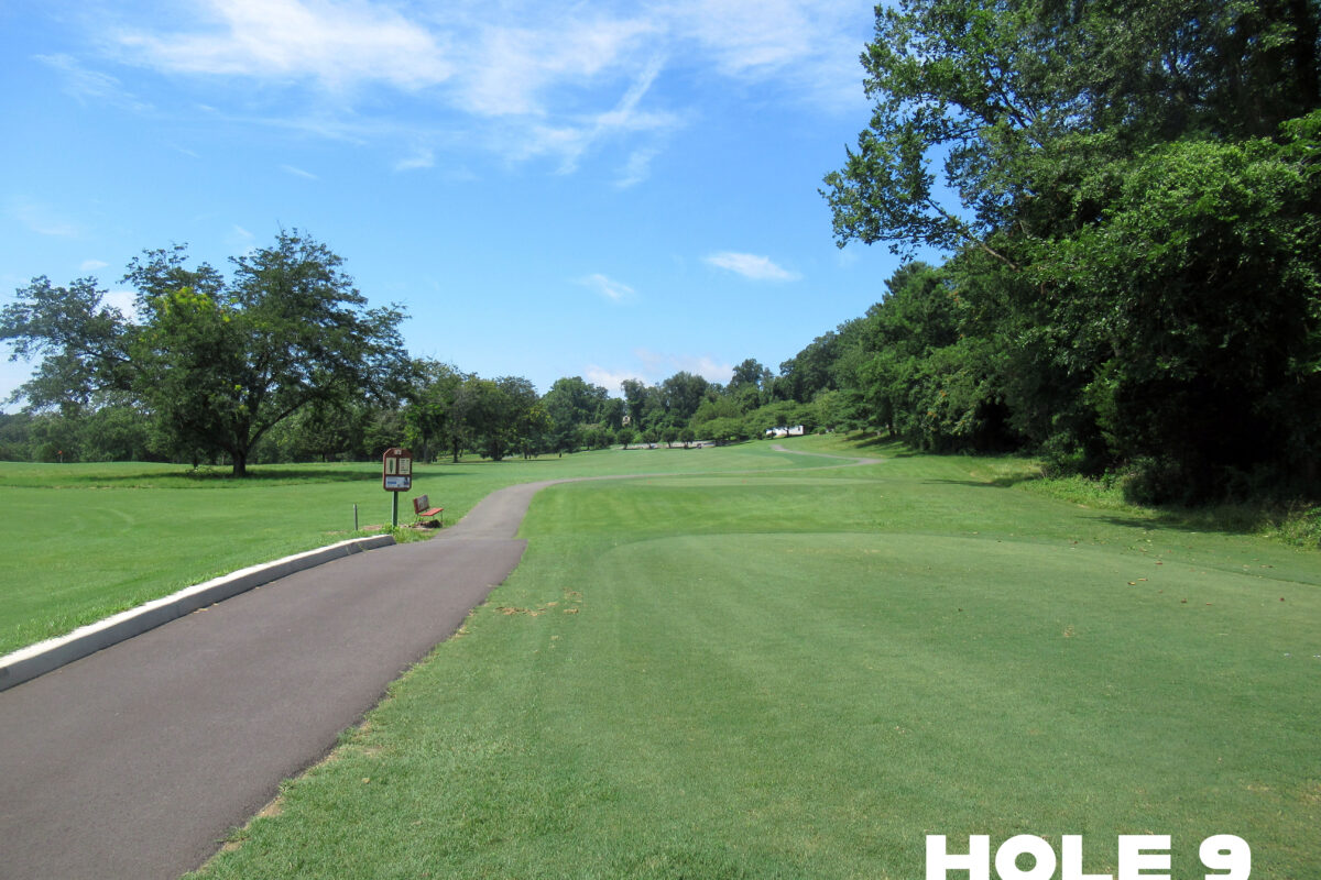 A smooth, paved path runs through a sloping grassy area with trees to the right and in the distance. In the foreground on the right is an elevated, leveled green. The words HOLE 9 are superimposed on the photo.