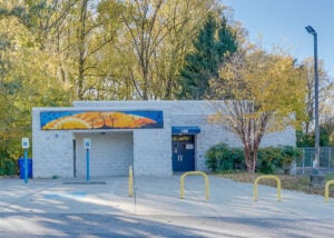 Exterior view of a single-story cinderblock building with a blue and gold sunrise mural on one wall.