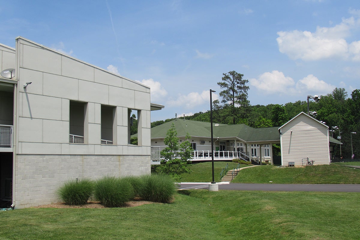 A road leading past a building with a long, covered entryway, a green roof, and beige siding.