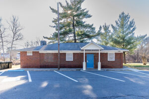 Front exterior view of a single-story brick building with a portico over a blue door.