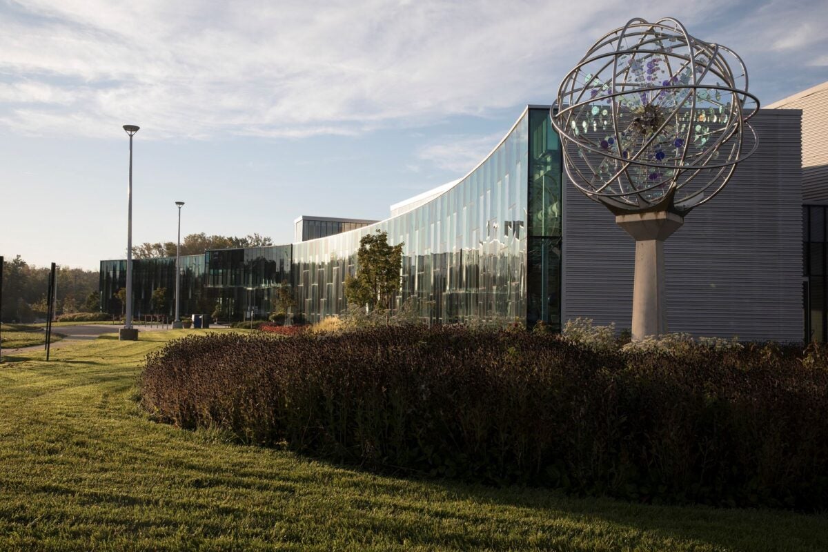 A large, glass and concrete building. Next to the corner of the building is a tall, spherical sculpture on a post.