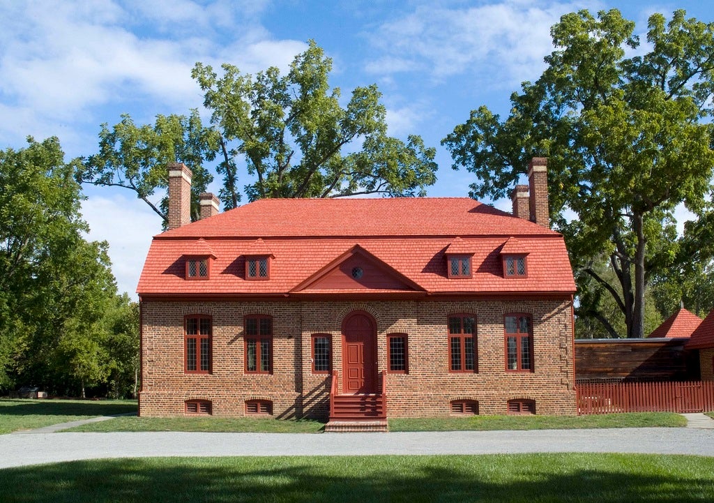 A two-story brick building with a red door, red trim, and a red mansard roof.