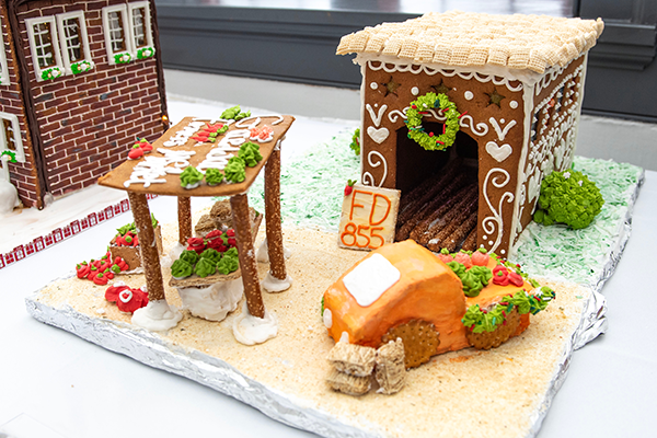 A gingerbread farmers market building with frosting and winter decorations lining the sides and a roof made of Rice Chex. The pretzel market stall is ready to sell all sorts of goods to gingerbread patrons.