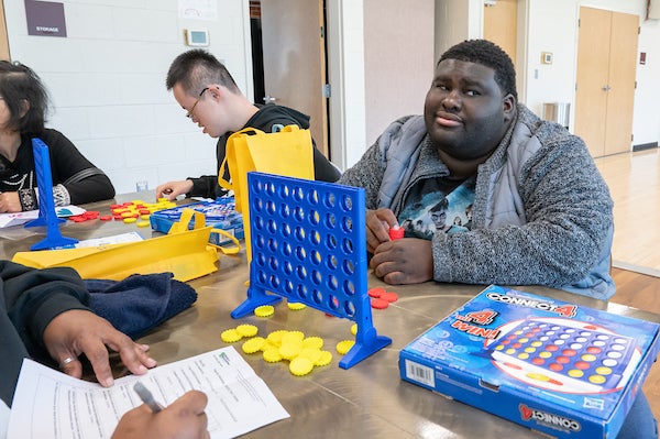 Four people play Connect Four at a table in a classroom.