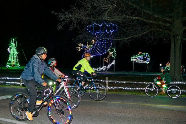 Group of three on bikes passing whale made of holiday lights.