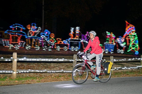 Person on bike in red sweater passing train made of holiday lights