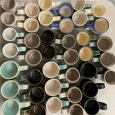 A collection of multi-colored ceramic mugs of various sizes and colors on a table