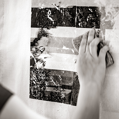A black and white image of a hand using a sponge to transfer color onto a surface