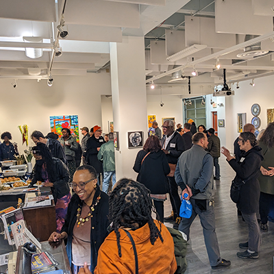 An art exhibition with white walls, wood floors, and many people observing the works of art