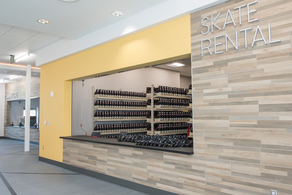 A large counter labeled SKATE RENTAL, with sets of ice skates sitting on the counter and visible by the hundreds on tall rows of shelves inside the skate rental area.