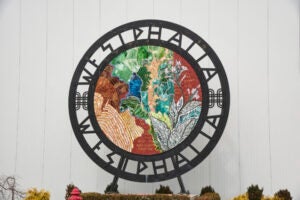 Circular artwork that reads WESTPHALIA around the top and bottom. Inside the circle is a colorful artwork or mosaic with leaves and flowers.