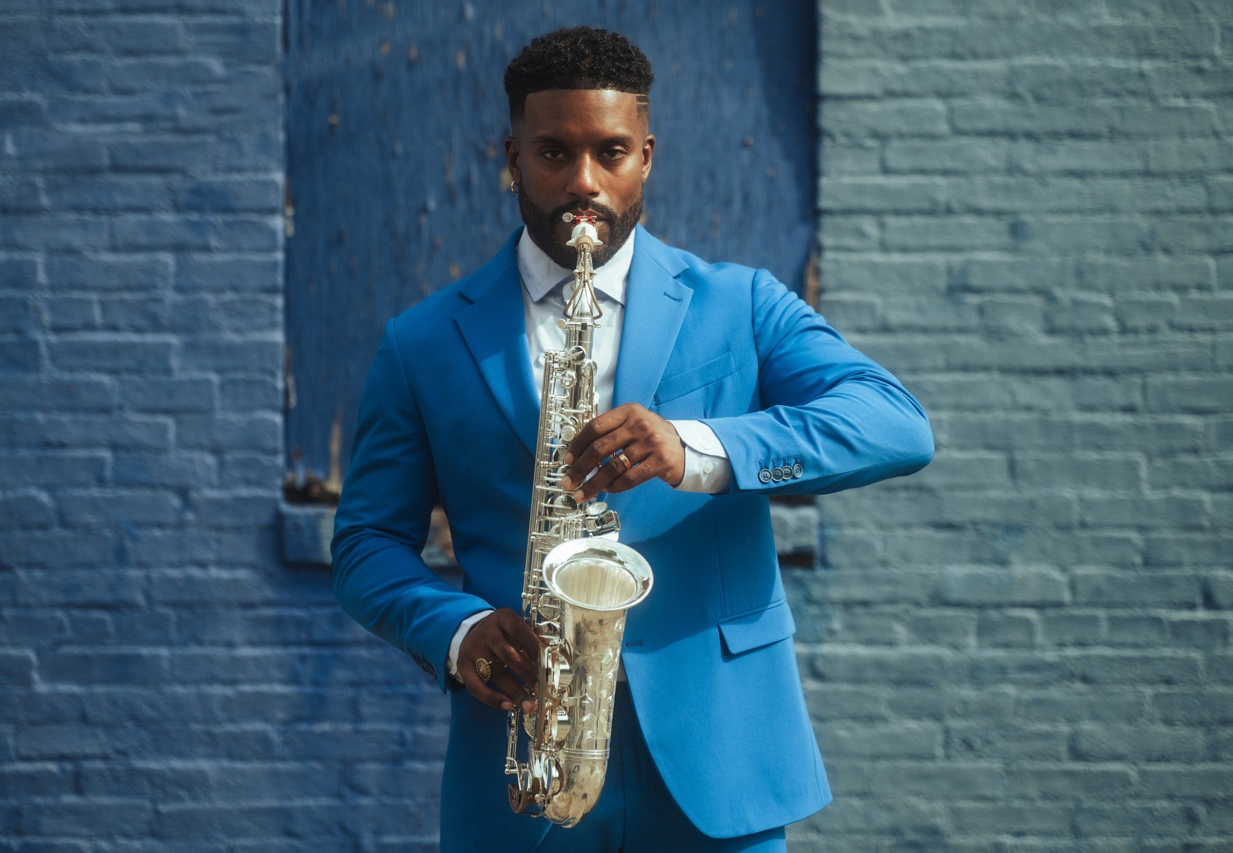Man in a blue suit playing a silver Alto Saxophone