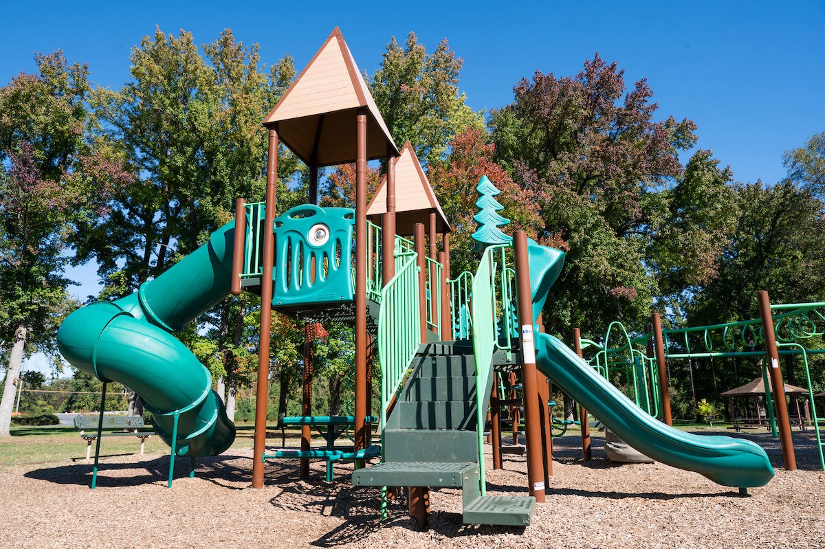 A playground with a large play structure featuring slides, platforms, towers, stairs, monkey bars, and benches. A picnic shelter is nearby.