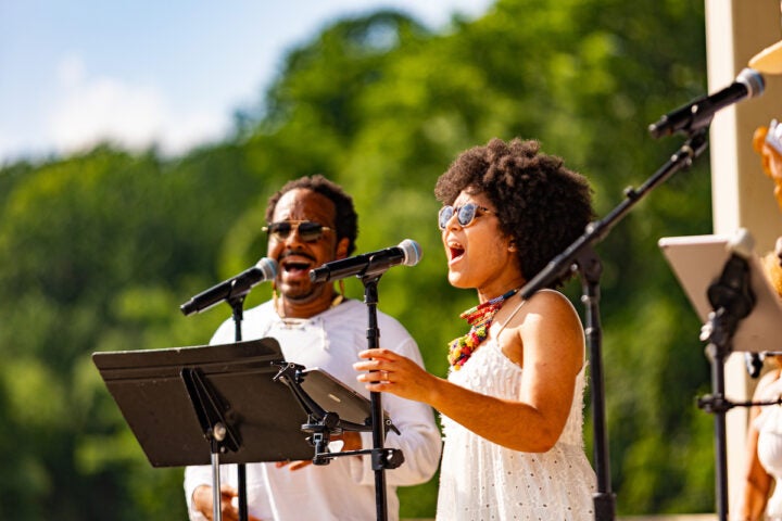 A man and a women singing into a mic outdoors.