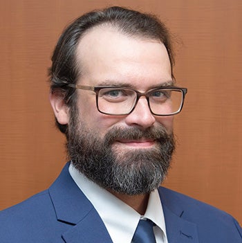 Headshot of a smiling man wearing glasses and a blue suit and tie.