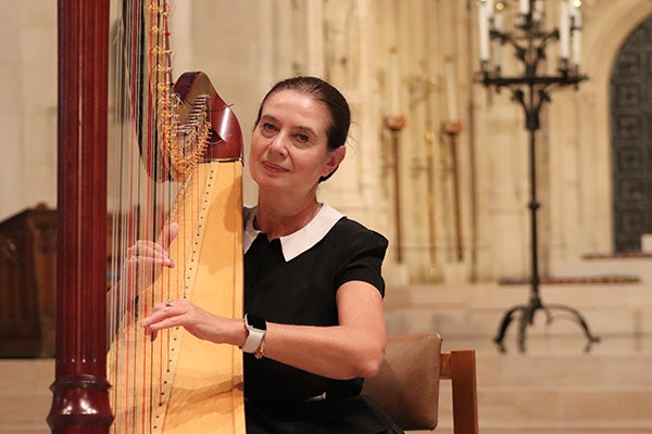 A seated woman plays a harp in a stone church or cathedral hall.