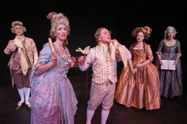 Five performers in elaborate, 18th-century costumes and wigs act on a stage.