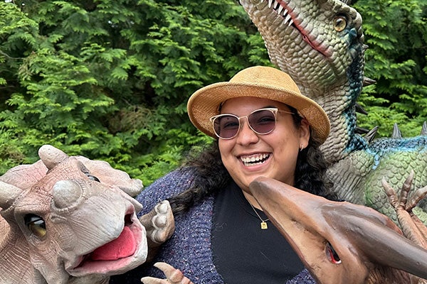 A laughing woman poses with several large, detailed dinosaur puppets.