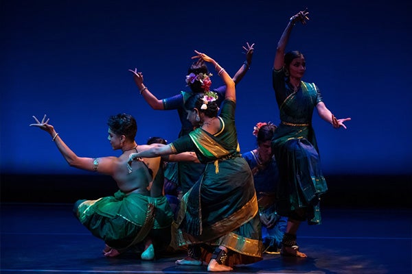 Six dancers in south Asian costumes perform on a stage.