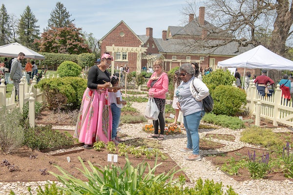 Visitors explore an herb garden during an outdoor festival at a historic estate.