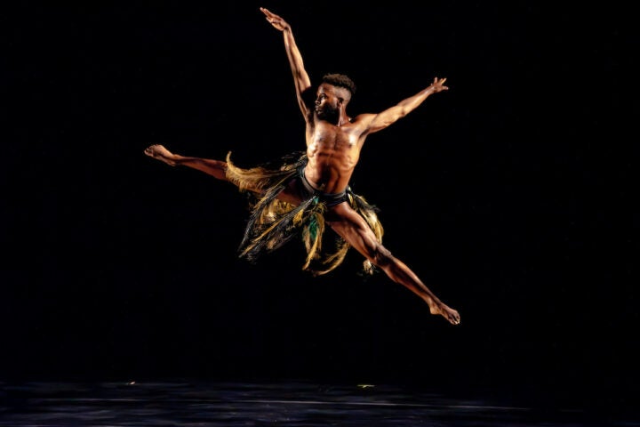 Male dancer in a costume with feathers jumps and dances on stage.