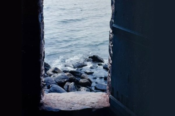 Waves of water lapping up on rocks, seen through a rough stone window.