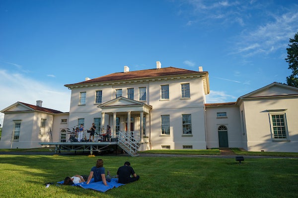 Outdoor concert at Riversdale House Museum, with attendees seated on a lawn facing a stage beside the historic mansion.