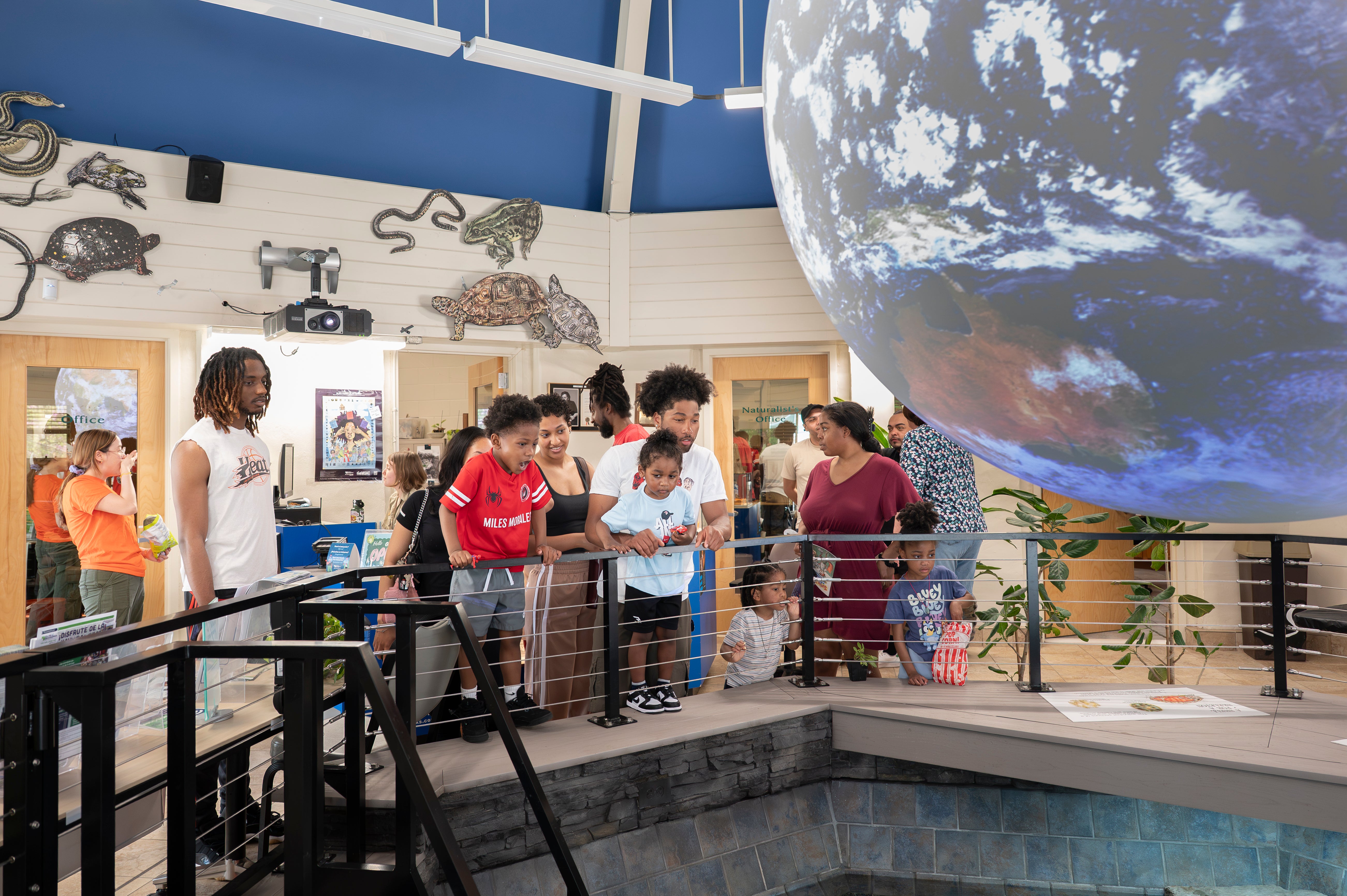 Museum visitors gather around a large suspended globe exhibit, viewing interactive displays and educational exhibits inside a nature center.