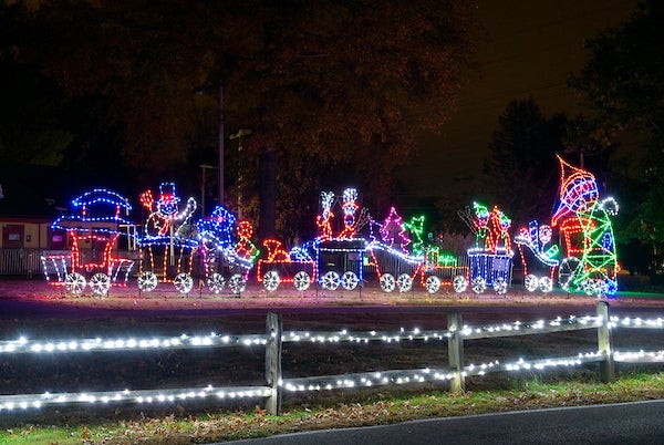 At night, a road runs past a festive holiday light display depicting a train loaded with toys and holiday items.