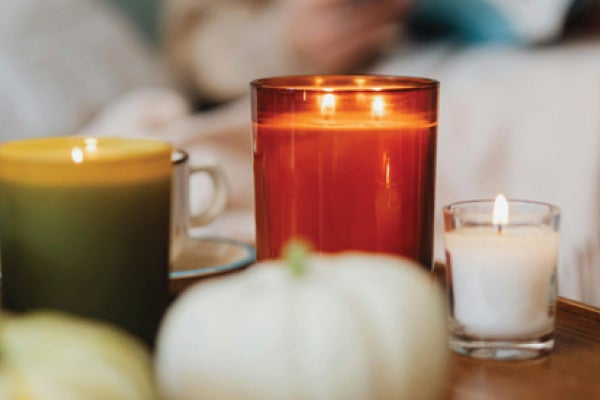 A collection of candles burning on a table. There are a few decorative pumpkins next to the candles