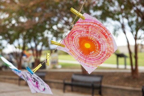 In a park, several spun paint artworks hang on a clothesline to dry.