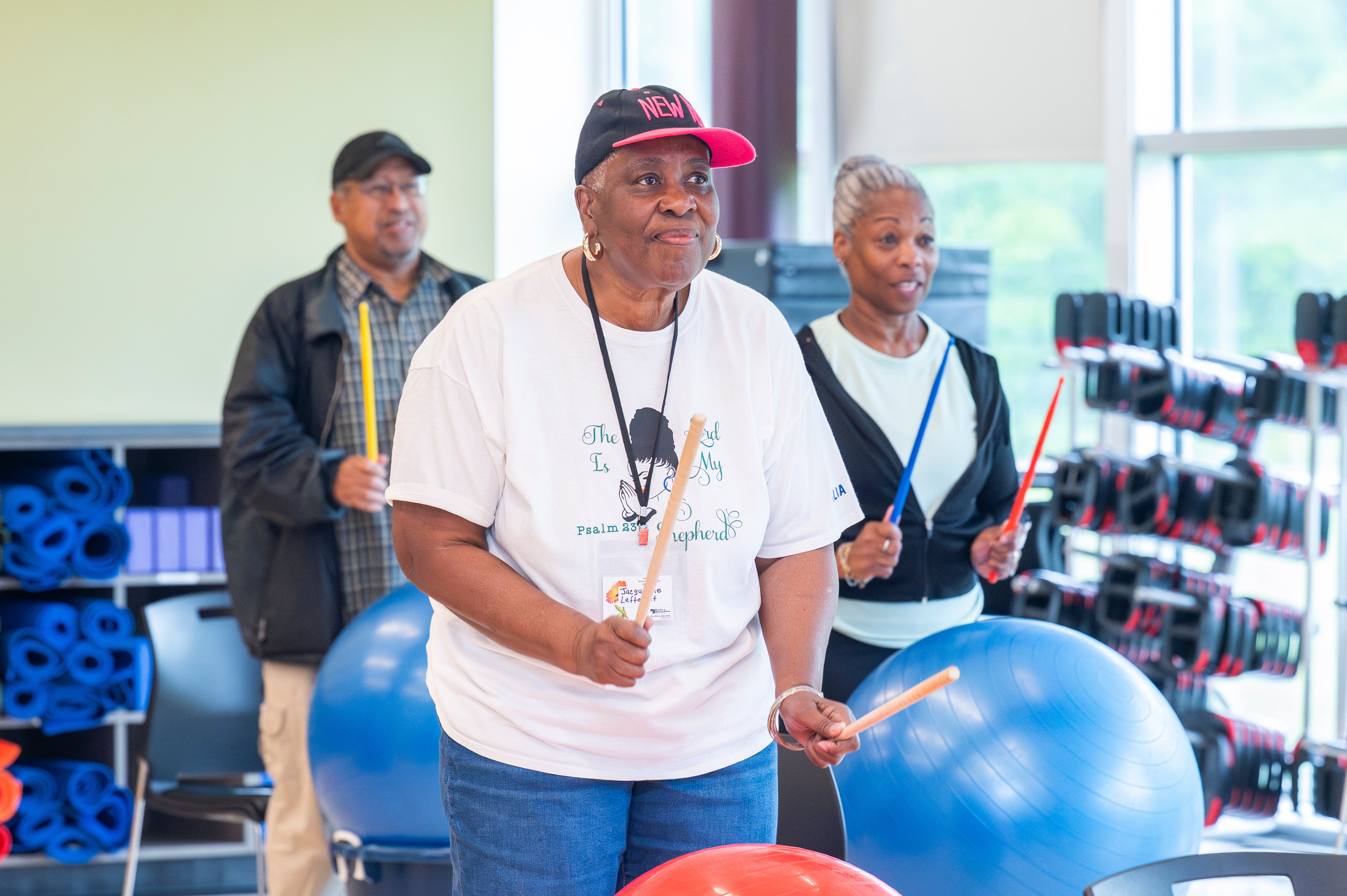 Older adults holding drumsticks and playing drum fitness on large blue and red stability balls during a workout class.